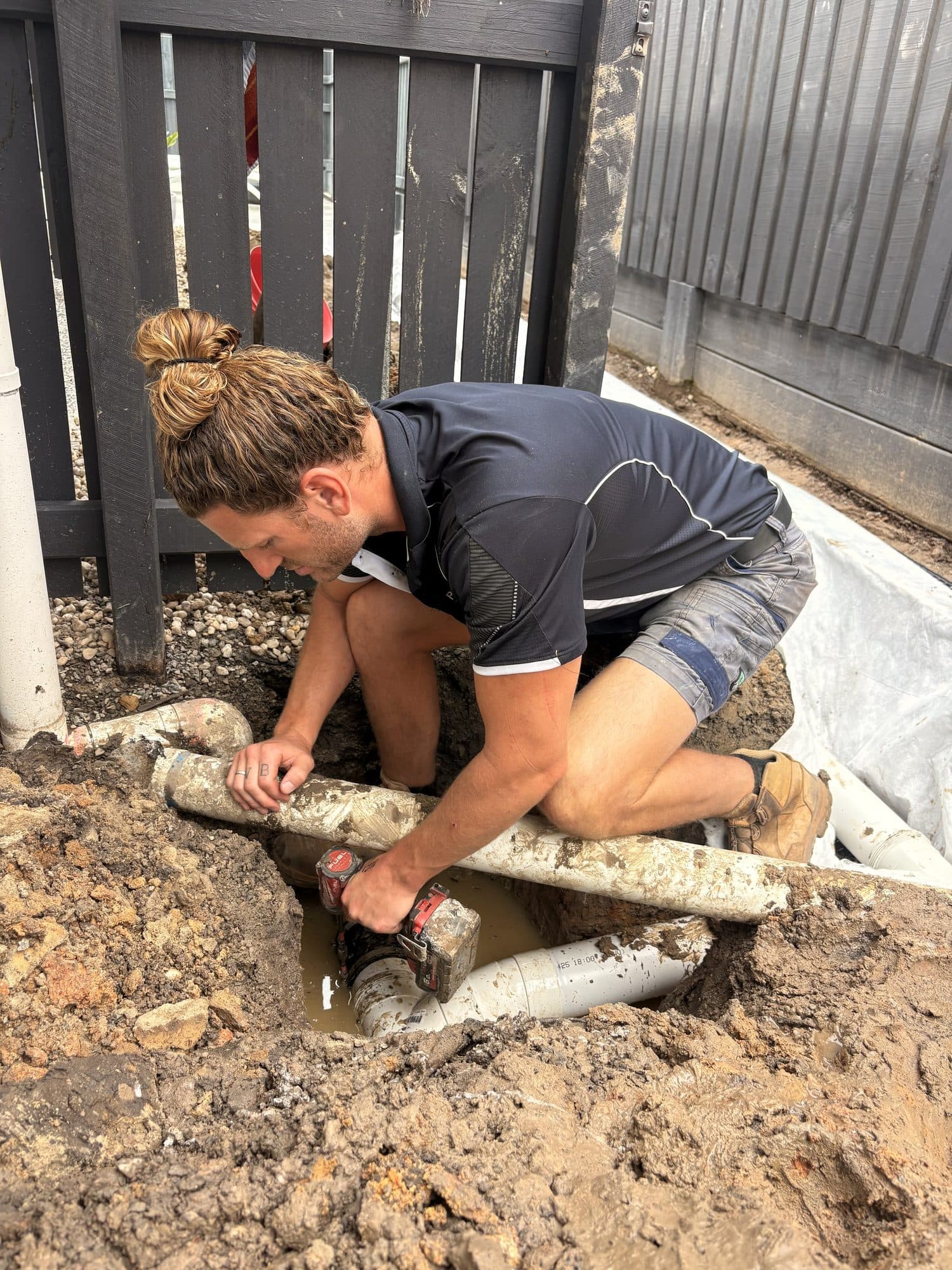 Rusty kneeling in mud to repair a buried PVC drain pipe